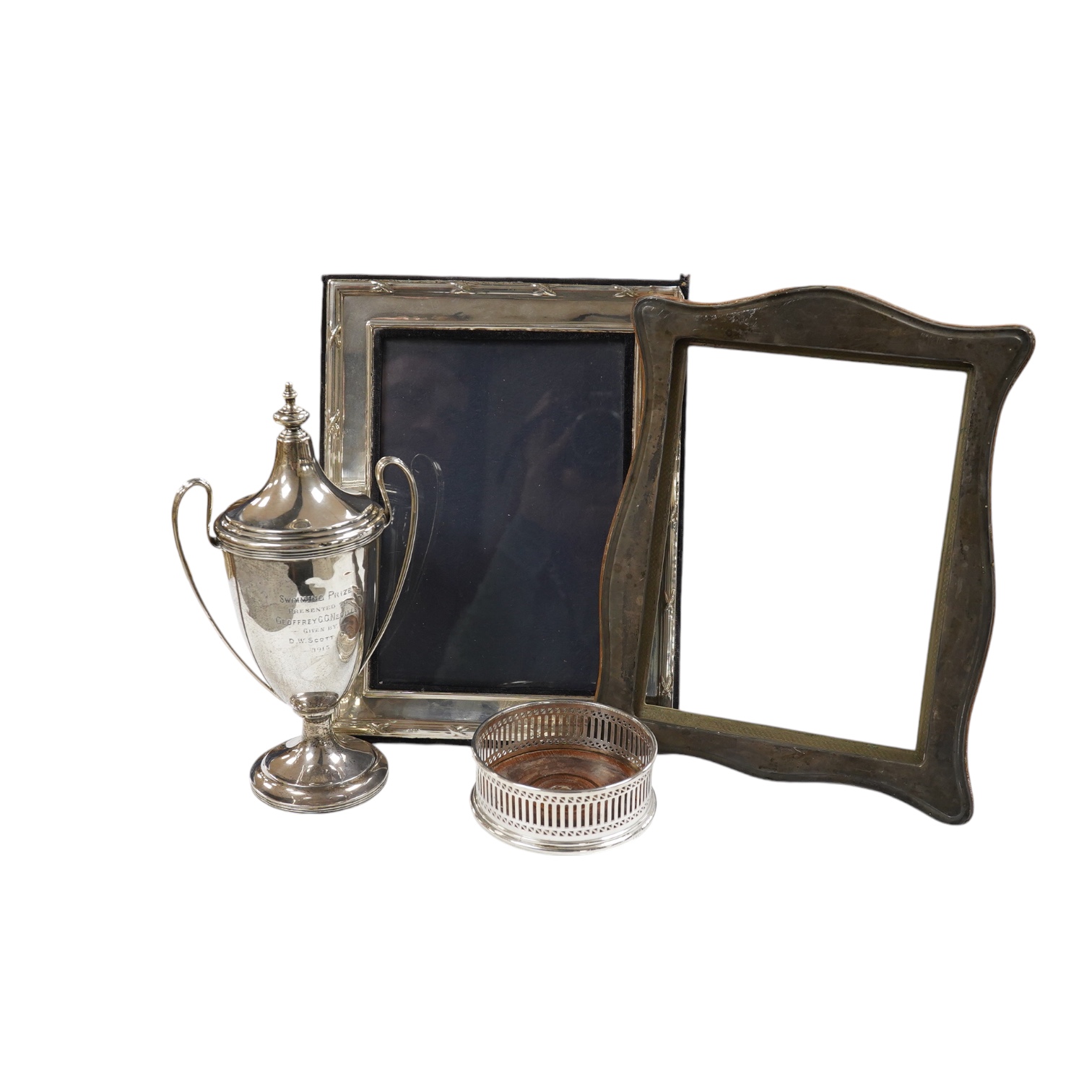 A George V silver two handled presentation trophy cup, 21.8cm, a modern silver wine coaster, a modern mounted silver photograph frame and a George V silver mounted photograph frame. Condition - poor to fair              