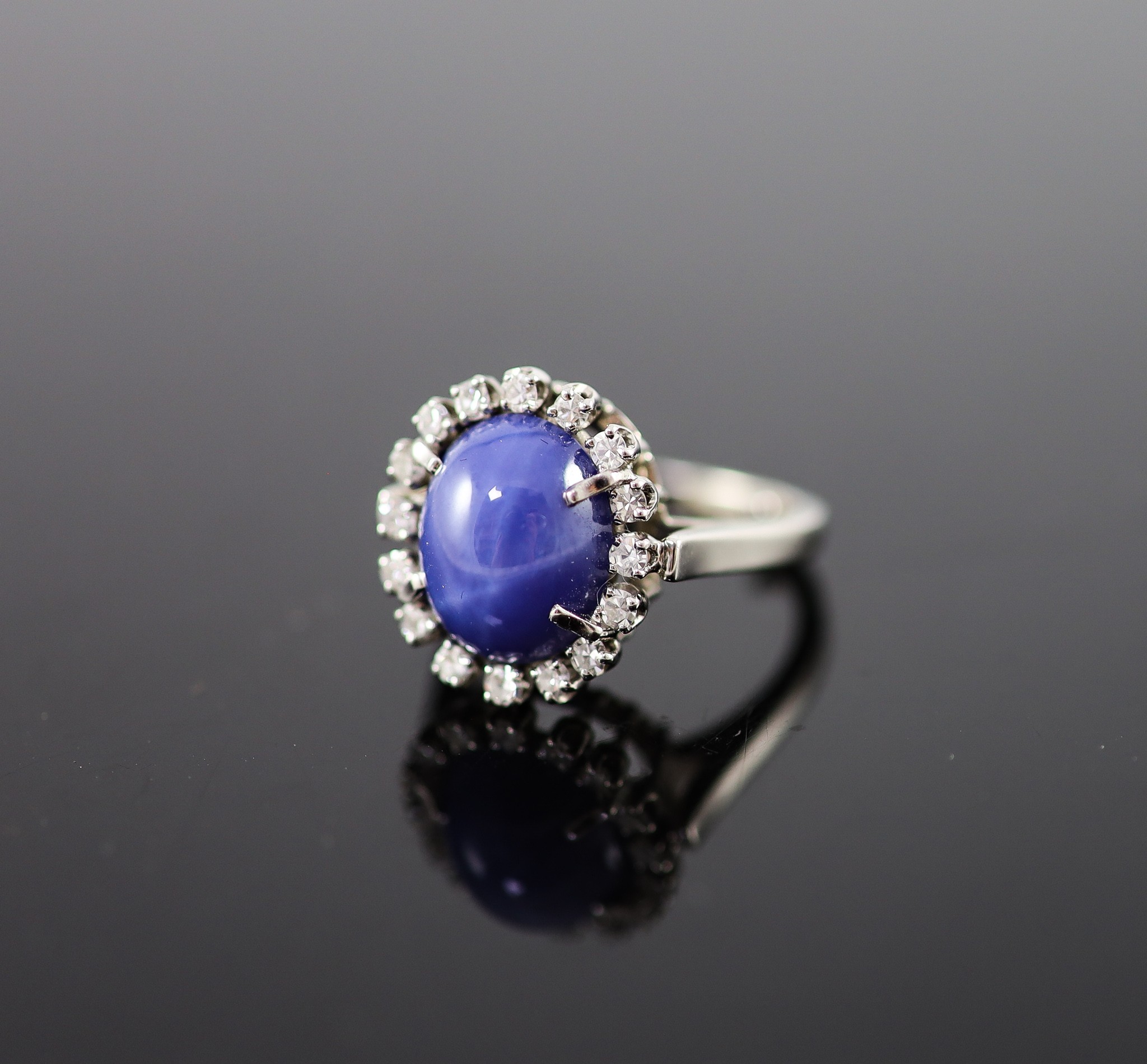 A 14k white gold, cabochon star sapphire and diamond set oval cluster ring                                                                                                                                                  