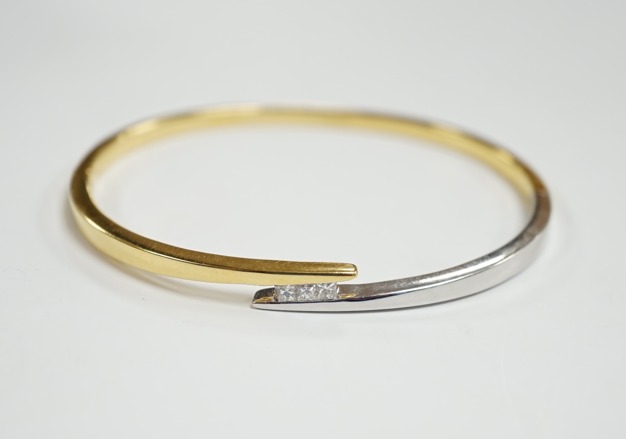 A modern two colour 18k and three stone princess cut diamond set hinged bangle, interior 60mm, gross weight 23.4 grams.                                                                                                     