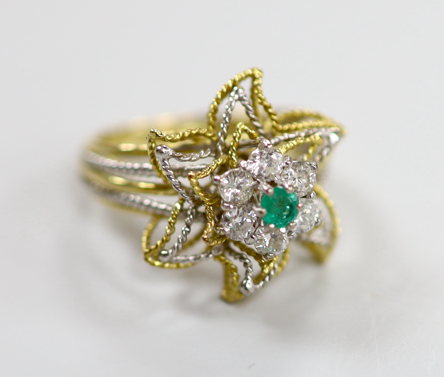 A yellow and white metal, emerald and diamond cluster set stylised flower head ring, size P, gross weight 6.3 grams.                                                                                                        