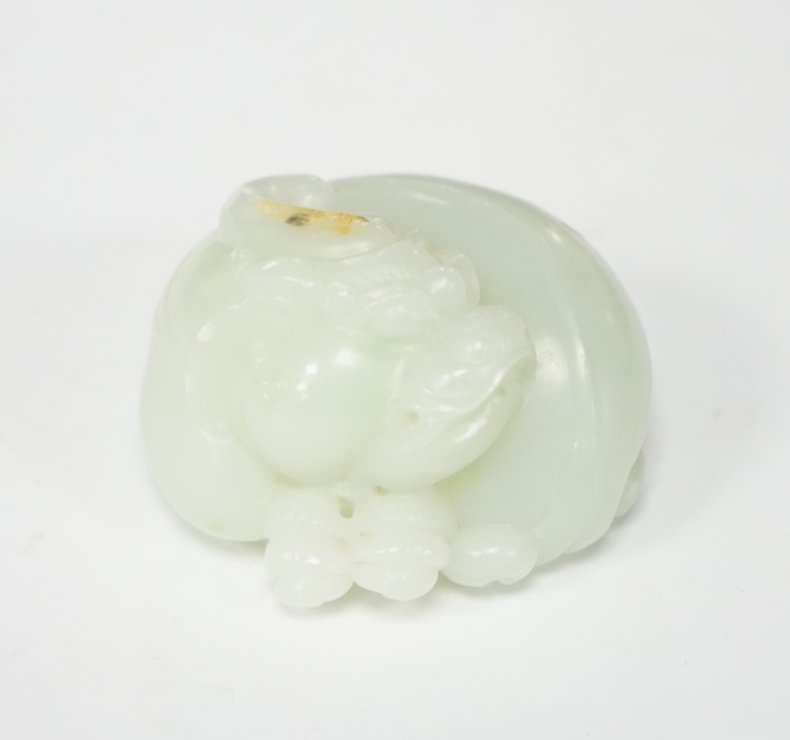 A Chinese celadon jade carving of a lion-dog, in recumbent pose, its crest with a russet inclusion, 5.3cm                                                                                                                   
