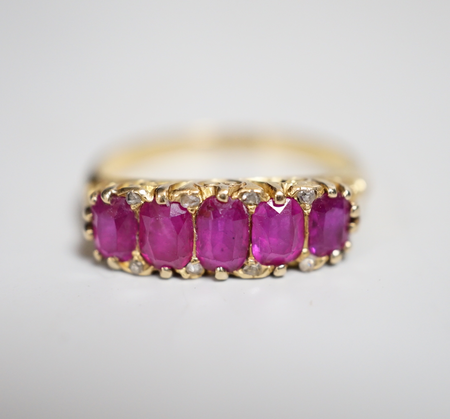 An early to mid 20th century 18ct and graduated five stone ruby set half hoop ring, with diamond chip spacers, size L, gross weight 3.5 grams.                                                                              