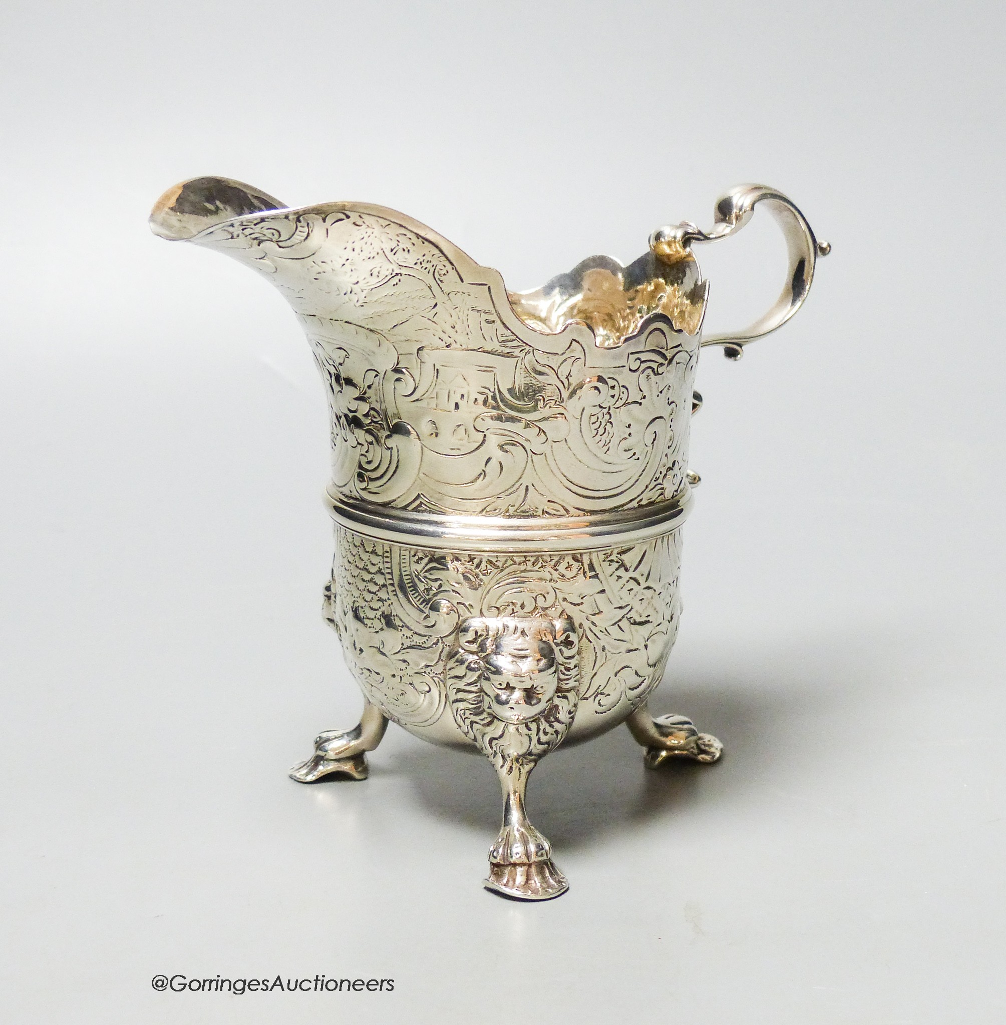 An engraved white metal helmet shaped cream jug, on tripod feet, unmarked, 12.9cm, 9oz.                                                                                                                                     