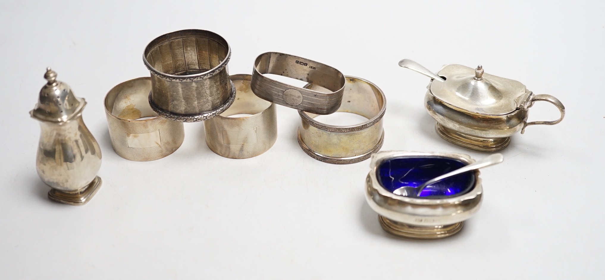 Five assorted silver napkin rings and a George V silver three piece condiment set.                                                                                                                                          