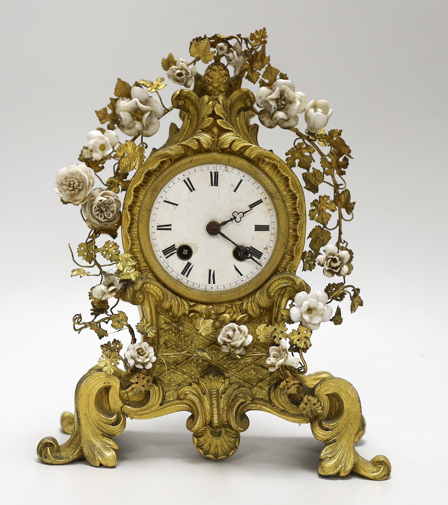 A 19th century gilt bronze and porcelain mounted mantel clock, the waisted case cast with rocaille, embellished with porcelain flower heads, with circular white enamel Roman dial, the associated twin train movement with 