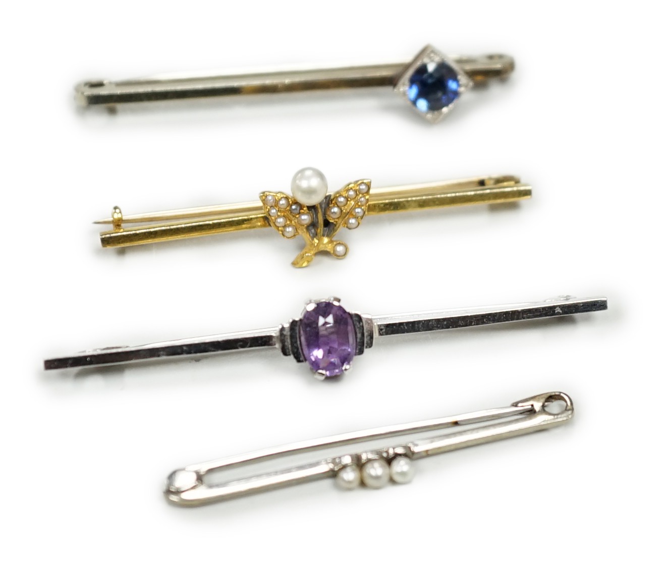 A 9ct white gold and synthetic? sapphire set bar brooch, 45mm and three other bar brooches including yellow metal and seed pearl, white metal and seed pearl and a 9ct and amethyst bar brooch, gross weight 8.1 grams.     