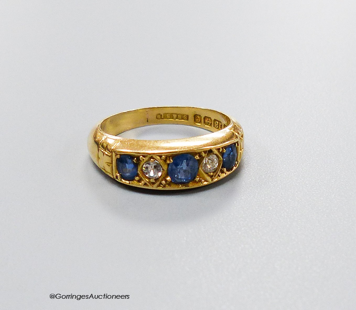 An Edwardian 18ct gold three stone sapphire and two stone diamond set half hoop ring, size M, gross weight 4.3 grams.                                                                                                       