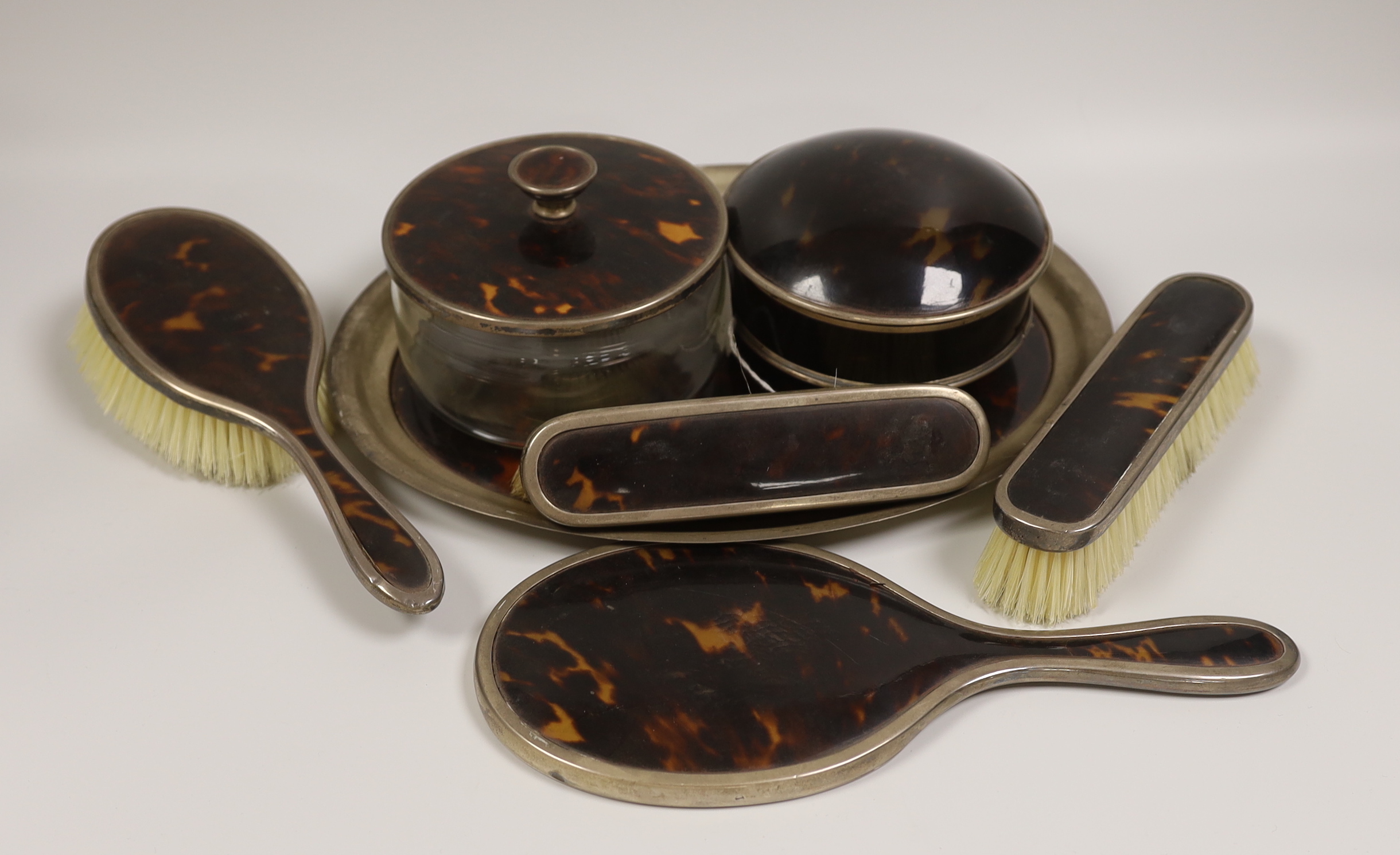 A matched George V silver and tortoiseshell mounted seven piece dressing table set, including a trinket box.                                                                                                                