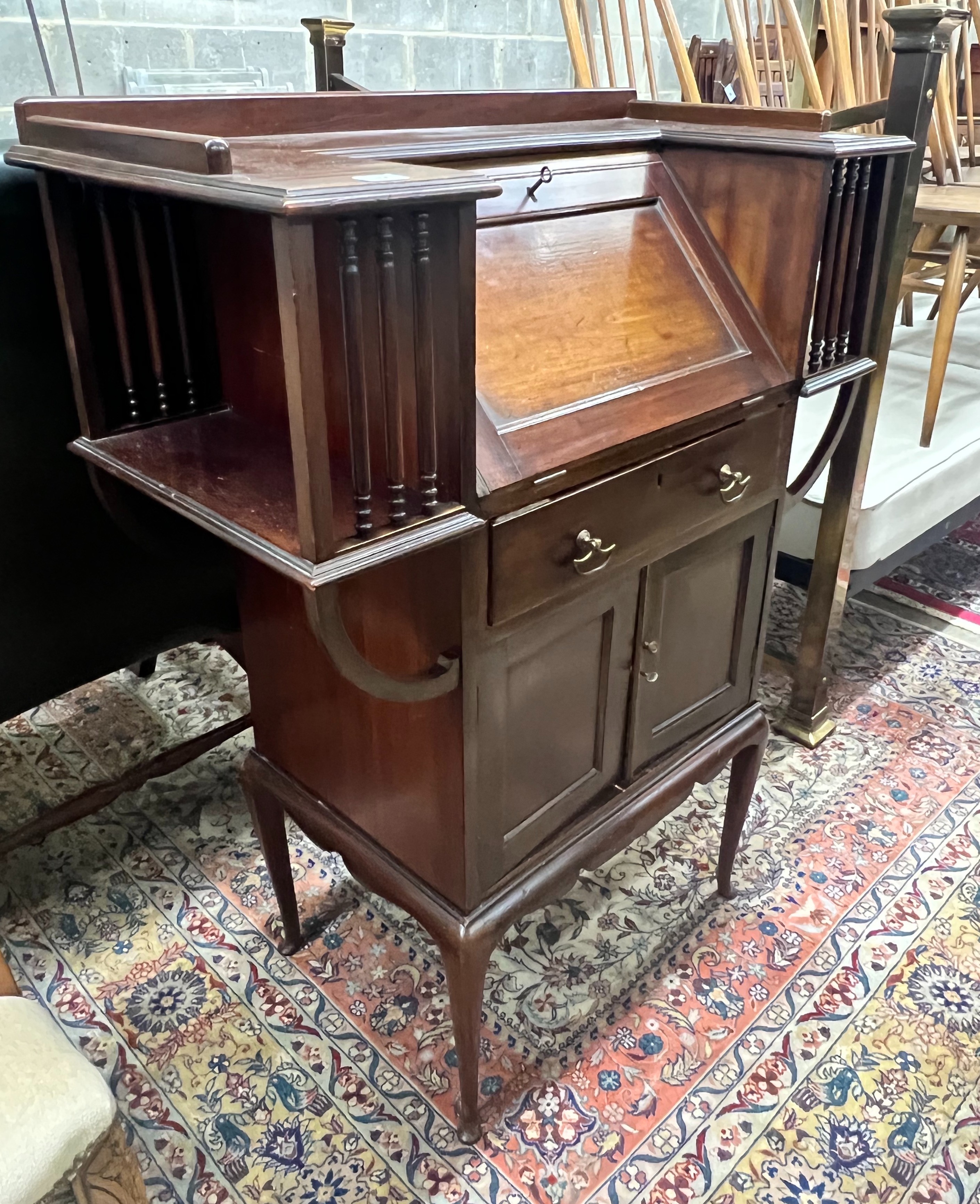 A late Victorian mahogany bureau, rectangular top with moulded ledge back and inset panelled writing slope, projecting bookshelves to the sides spaced with turned supports‘ drawers and cupboard doors, on cabriole support