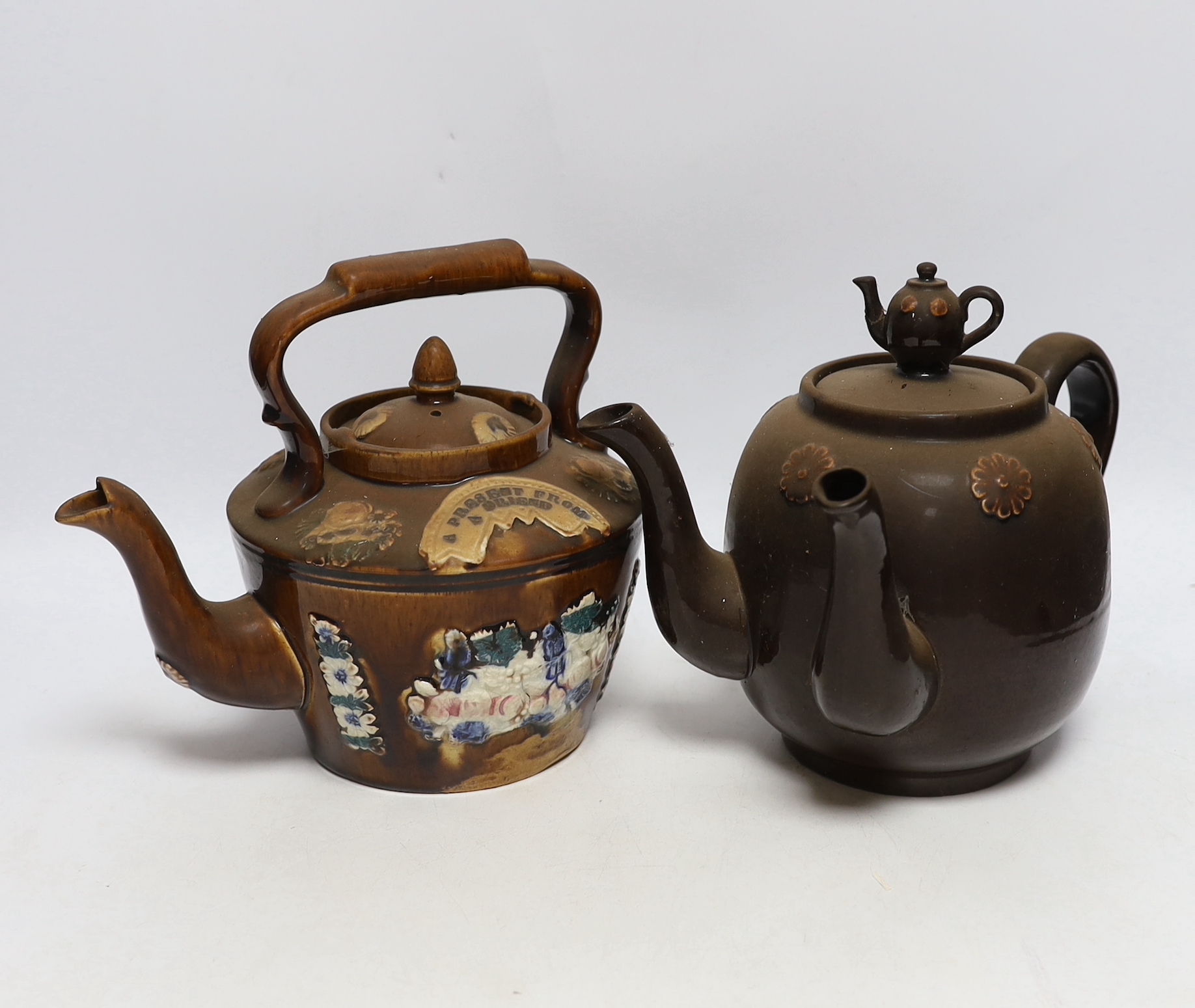 Two Measham Barge ware glazed pottery teapots, decorated in relief, largest 24cm wide                                                                                                                                       