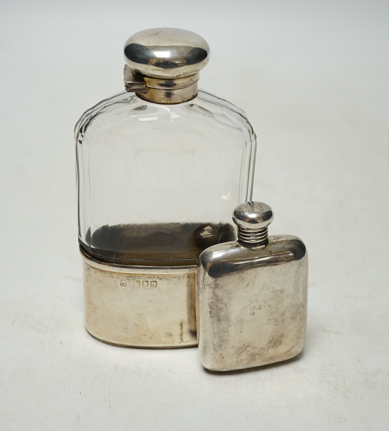 An Edwardian silver mounted glass hip flask, London, 1902, 14cm, together with a small George V silver hip flask by A & J Zimmerman & Co. Condition - fair                                                                  