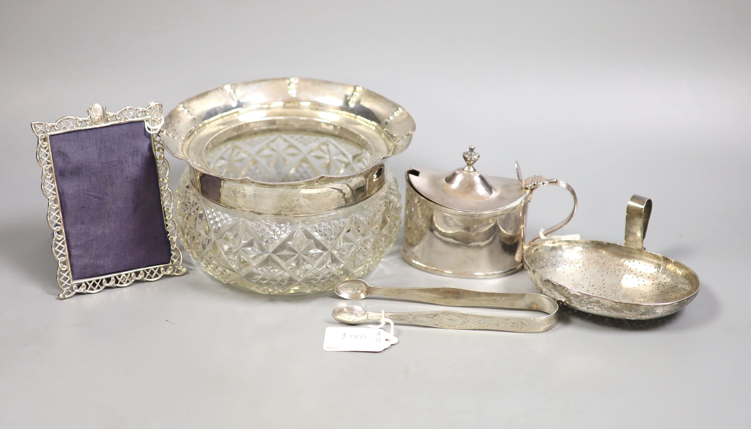 A small selection of decorative silver items to include a Georgian pierced strainer, a mustard pot, pair of sugar tongs and a mounted glass jar (lacking cover).                                                            